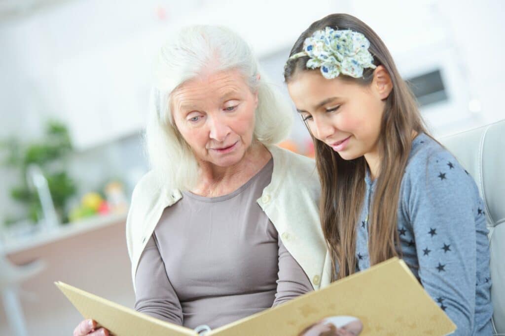 A grandmother sitting on a cough with a young lady holding a book