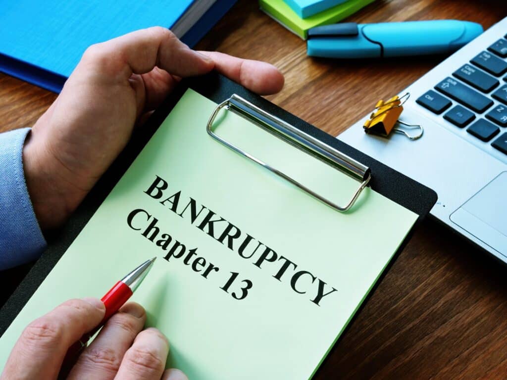 Hand holding a pen and clipboard that says bankruptcy chapter 13